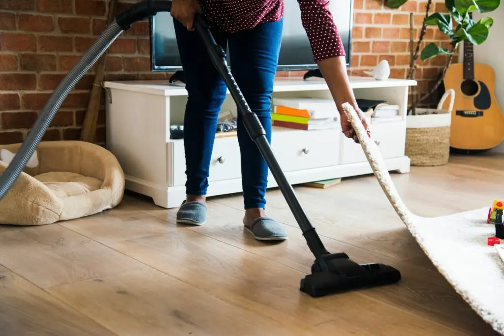 Person vacuums a living room with a brick wall, white cabinet, and guitar in the background (action: cleaning).