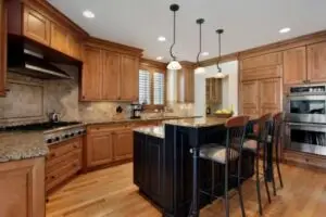 Kitchen with warm wood cabinets, granite countertops, a black island with seating, and pendant lights; stainless steel range and wall ovens nearby.