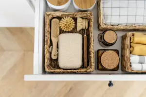 Zero waste products inside organization boxes on kitchen | House Cleaning Rapid City South Dakota Open bathroom drawer with woven baskets holding soap bar, sponge, wooden brush, cotton pads, and rolled towels.